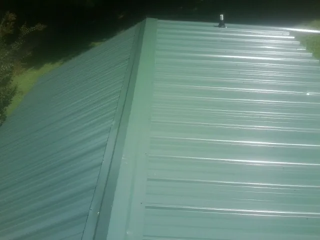 New green metal panels meeting at the ridge of a roof — Flat Roof Repair work by our crew in Laurel